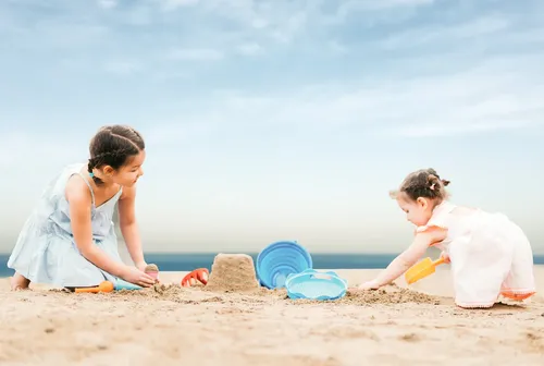 ילד/ה משחק/ת בהנאה עם דלי חוף כחול מתקפל של CompacToys בחול ים