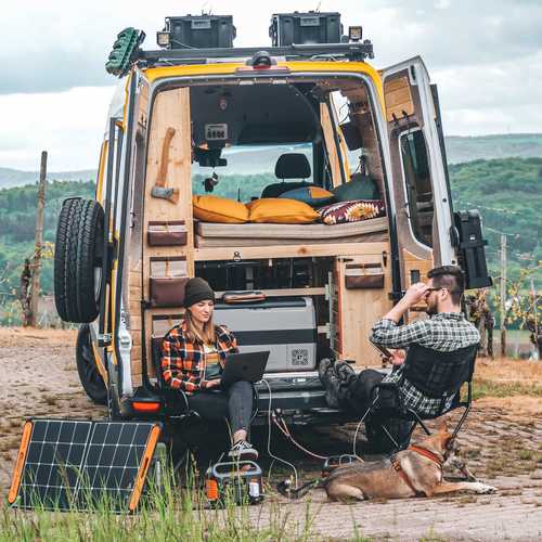 תחנת כוח ניידת Jackery Explorer 500 בצבע שחור-כתום עם ידית נשיאה גדולה, מסך LCD מרכזי, מתגי הפעלה נפרדים ומגוון יציאות כולל AC, DC ו-USB. התמונות מציגות 3 דרכי טעינה שונות וחלוקת יציאות מפורטת עם זמני טעינה לכל מקור