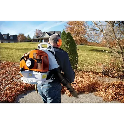 אדם עם אוזניות מגן משתמש במפוח גב STIHL BR 430 לפינוי עלים בשביל גישה סמוך לבית כפר
