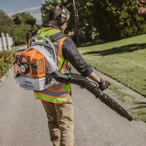 גנן מקצועי לבוש אפוד זוהר משתמש במפוח גב STIHL BR 430 לניקוי שביל בגינה ירוקה