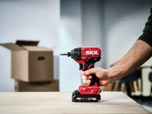 מברגת אימפקט נטענת SKIL 20V Brushless מונחת ביד המשתמש על משטח עבודה