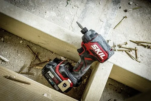 מברגת אימפקט נטענת SKIL 20V עם סוללת PWR CORE, מונחת באתר עבודה עם ברגים מסביב
