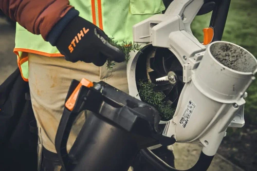 טכנאי עם כפפות STIHL פותח את בית הלהבים של שואב עלים SHA 140 לצורך ניקוי ותחזוקה.