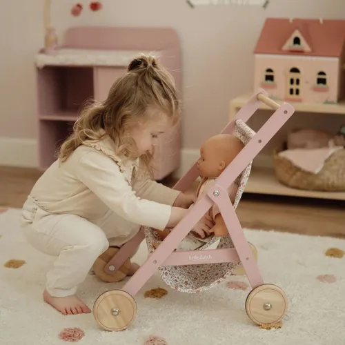 ילדה משחקת בעגלת בובה מעץ עם בובה בתוך העגלה, הילדה רוכנת לטפל בבובה
