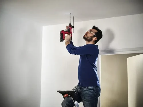 אדם עומד על סולם ומקדח בתקרה באמצעות פטישון נטען של SKIL
