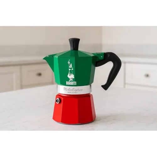 מקינטת Bialetti בצבע ירוק‑אדום מונחת על שיש מטבח בהיר עם רקע מטבח בהיר.