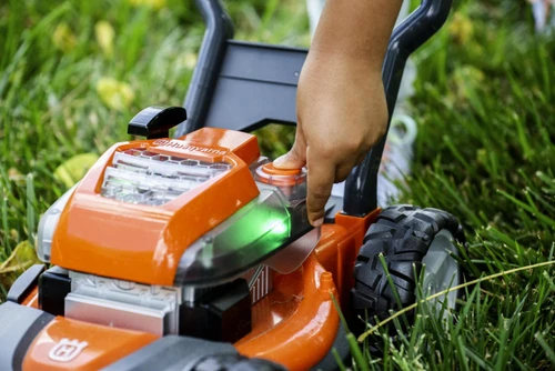 מכסחת דשא צעצוע לילדים בסגנון Husqvarna עם סוללה מדומה ולחצן הפעלה בגינה
