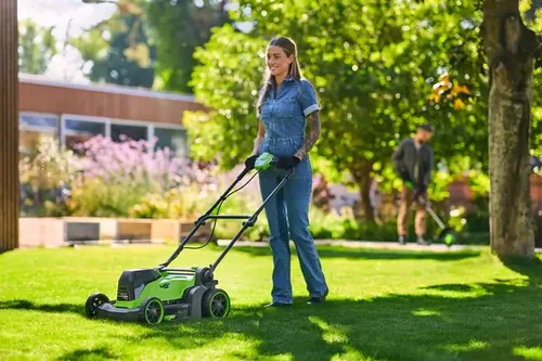 אישה משתמשת במכסחת דשא נטענת ירוקה 48V של Greenworks בגינה ירוקה רחבת ידיים