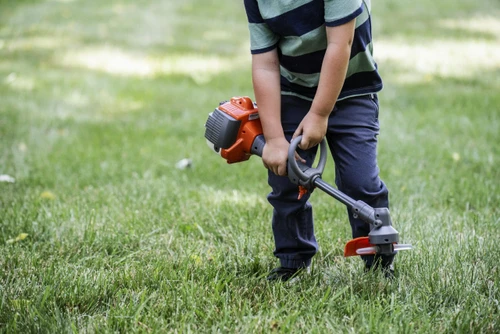 ילד משחק עם חרמש צעצוע Husqvarna Toy Trimmer על גבי דשא, כולל צלילי עבודה, תאורת LED וראש מסתובב לחוויית משחק מציאותית ומהנה לילדים מגיל 3 ומעלה