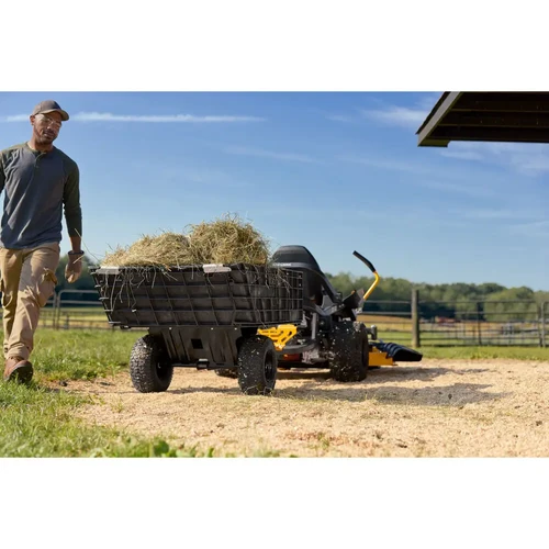 טרקטורון כיסוח דשא Cub Cadet ULTIMA Z3-60 גורר עגלת משא מלאה בחציר, מציג את יכולת הגרירה והעבודה המשקית של הכלי