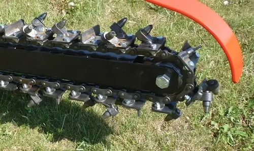 תקריב שרשרת החפירה המשוננת של טרנצר LASKI TR60/13HC, המציג שיני חיתוך מתכת, זרוע חפירה ומגן אדום לפינוי אדמה