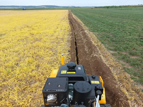 טרנצר LASKI TR60/13HC במהלך חפירת תעלה ארוכה וישרה בשטח חקלאי, מבט מעמדת המפעיל המציג את תוואי החפירה ופינוי האדמה לצדי התעלה